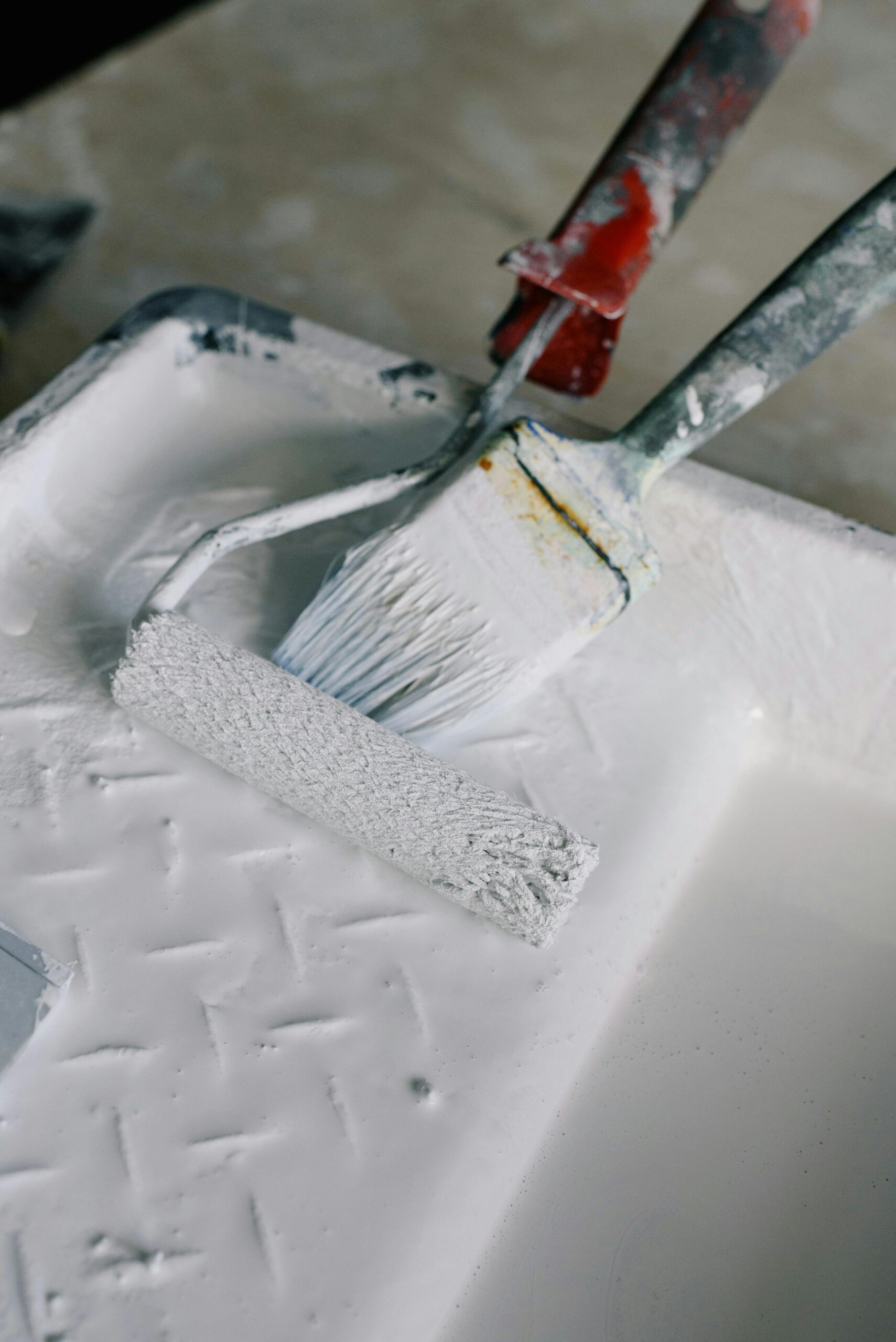 Close-up of paintbrushes and roller in a white paint tray for home renovation.